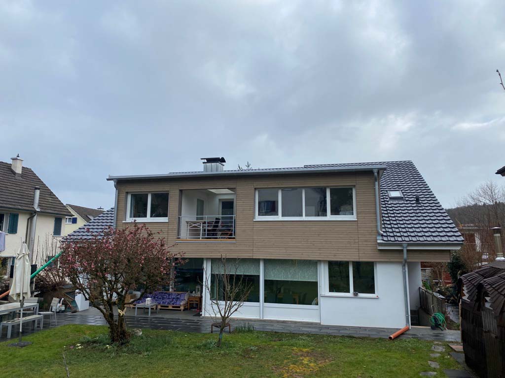 Haus mit Holzfassade, Balkon und Terrasse. Im Vordergrund der Garten.