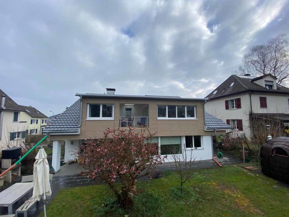 Haus mit Holzfassade, Balkon und Terrasse. Im Vordergrund der Garten.