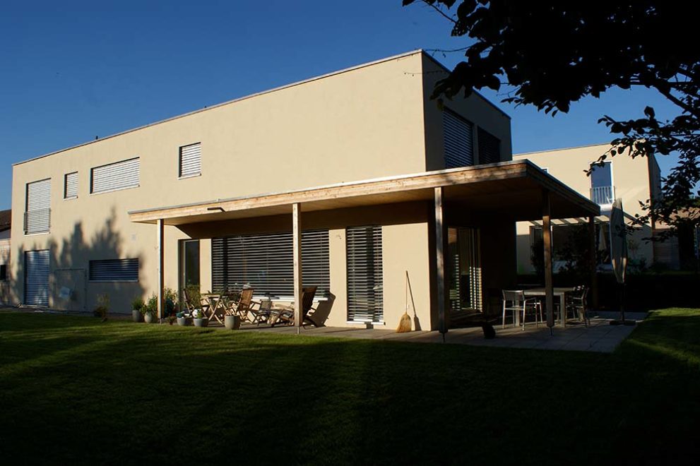 Haus mit gelber Putzfassade und großer Terrasse aus Sicht des Gartens