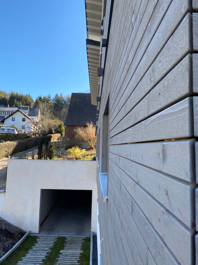 Nahaufnahme der Holzfassade eines Neubaus und Zugang zu einer Garage