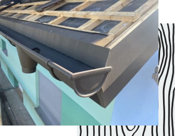 Graue Dachrinne an einem Wohnhaus mit mint farbener Fassade..