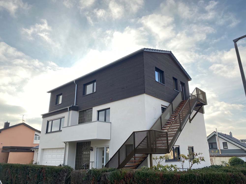 Weißes Haus mit teils hölzerner Fassade und großer Treppe um das Haus herum