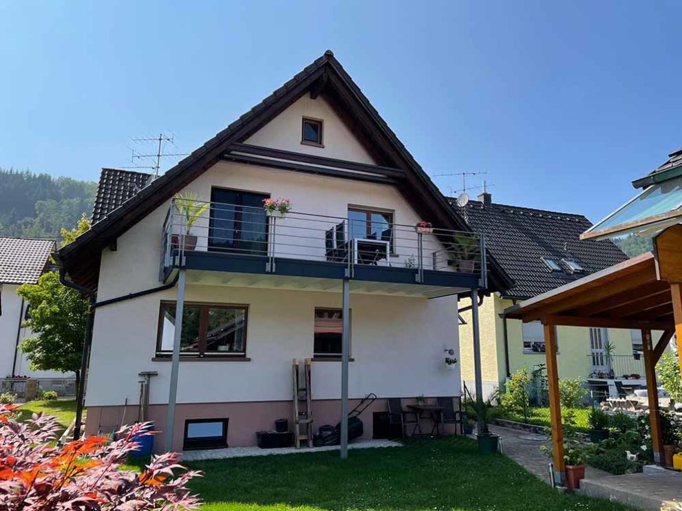 Weißes Haus mit Balkon und Garten, sowie Teil des Carports