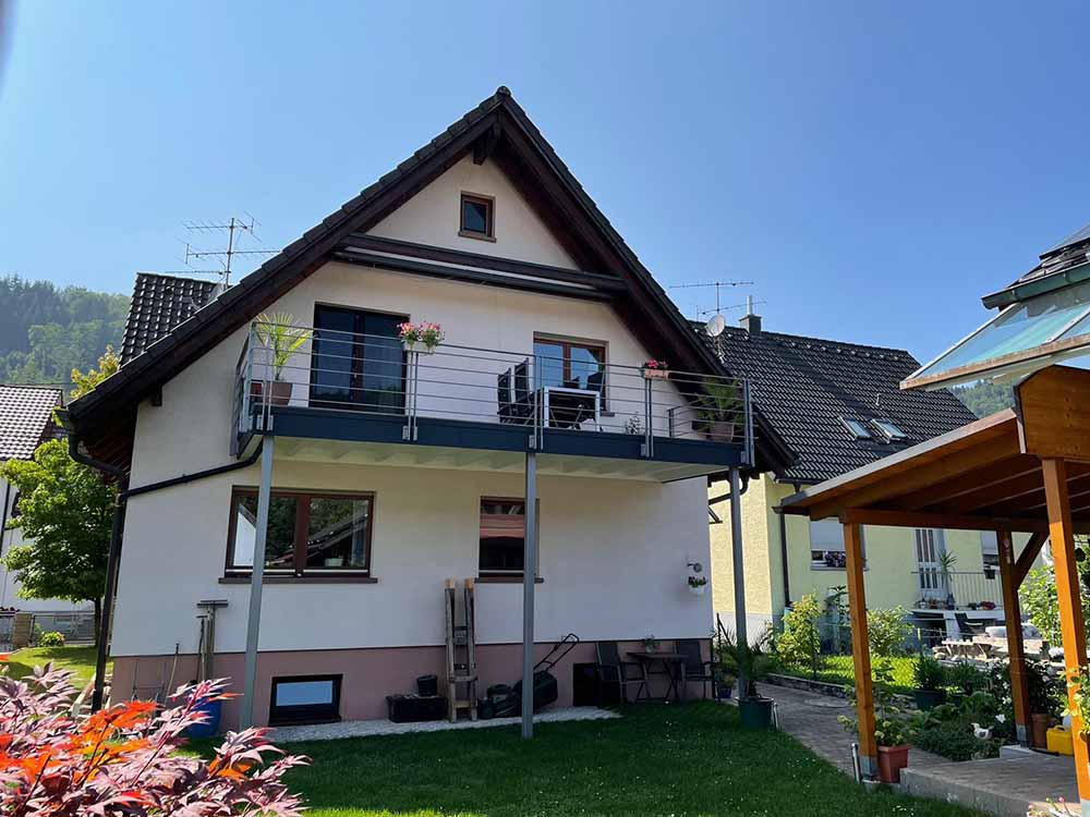 Weißes Haus mit Balkon und Garten, sowie Teil des Carports