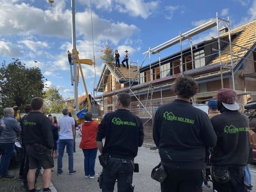 Arbeiter der Firma Kuri Holzbau feiern Richtfest, zwei Männer stehen auf dem Dach des Neubaus.
