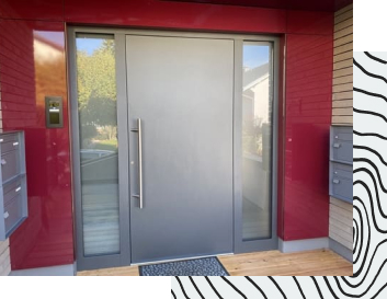 Granitfarbene massive Haustür, welche von einer roten Hauswand umrahmt ist.